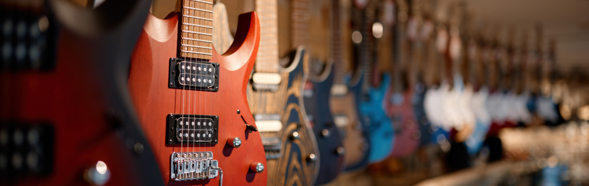 Electric guitars on the rack in a row at modern musical showroom. String music instrument hanging on ceiling waiting for buyer